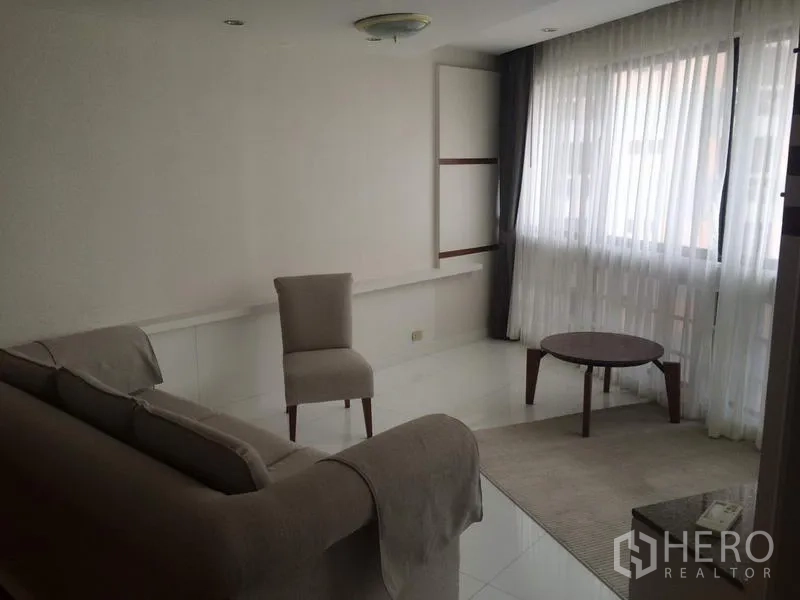 Condominium for rent in Khlong Toei, Bangkok - Bright secondary sitting room with sofa, accent chair and coffee table beside large sheer-draped windows at President Park.