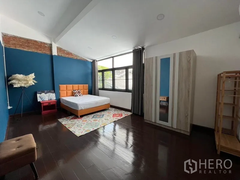 Townhouse for rent in Ratchathewi, Bangkok - Second bedroom with blue feature wall, large window, dark wood flooring and simple furniture.