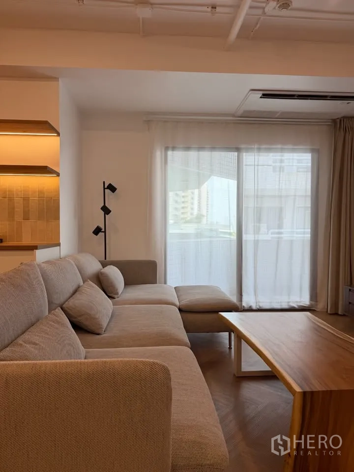 公寓 for rent in Watthana, Bangkok - 明亮客厅，L形沙发、原木茶几与通向阳台的推拉门。