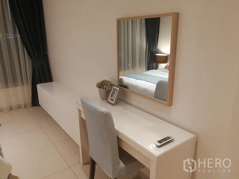 公寓 出租或出售在Watthana, Bangkok - 卧室梳妆区：白色书桌与镜子、长柜及纱帘靠窗。