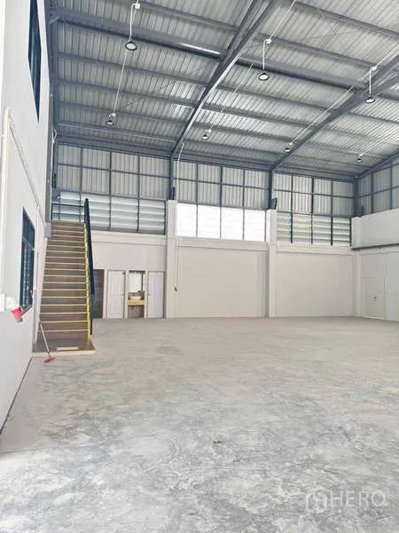 货栈 出租在Mueang Rayong, Rayong - 仓库内部挑高空间，混凝土地坪，带窗户和通往夹层办公室的楼梯。