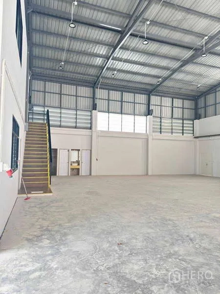 货栈 出租在Mueang Rayong, Rayong - 仓库内部挑高空间，混凝土地坪，带窗户和通往夹层办公室的楼梯。