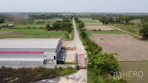 Warehouse for sale in Lam Luk Ka, Pathum Thani - Warehouse beside a long rural road with trailer access, surrounded by farmland.