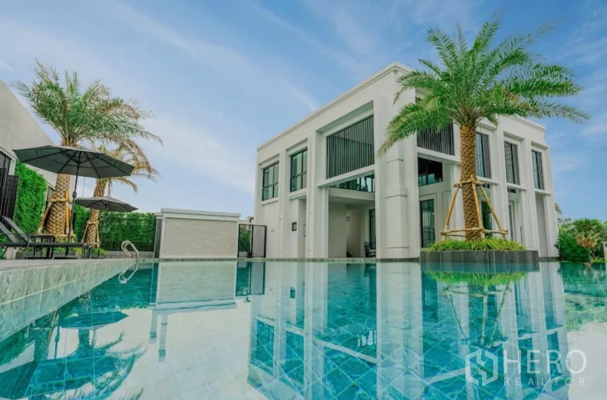 Townhouse for rent in Chatuchak, Bangkok - Turquoise pool beside white clubhouse framed by palm trees.