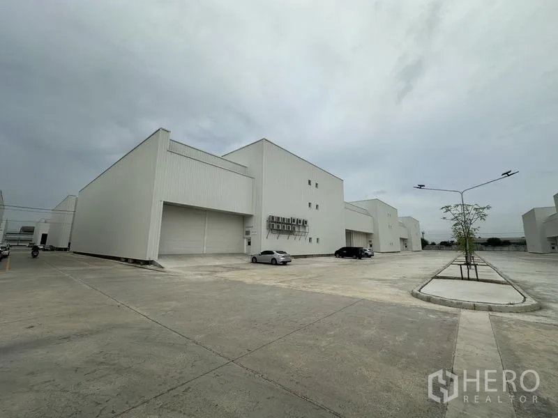 工厂 出租在Pathum Thani - 新建白色厂房外观，宽阔混凝土场地与停车位，位于工业园区。