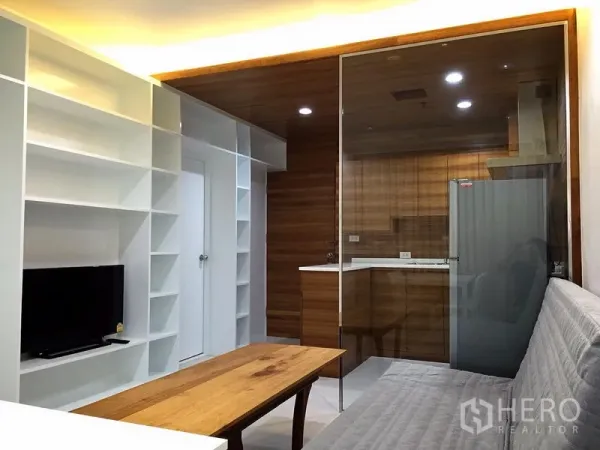 公寓 出租在Bang Rak, Bangkok - 温馨起居区，面向电视柜，玻璃墙连接木质厨房，配嵌灯。
