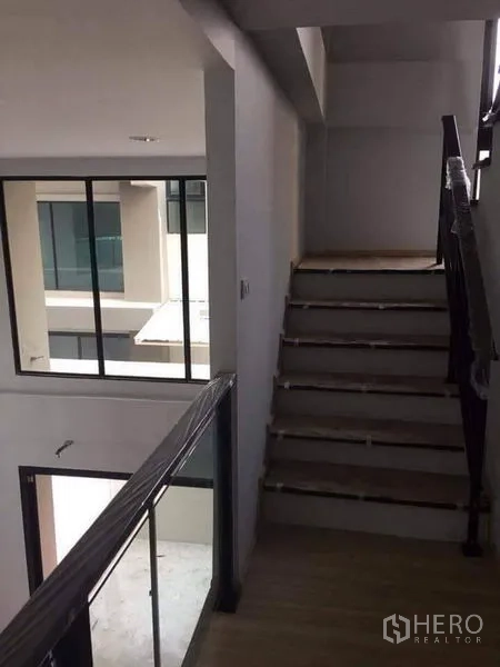 Townhouse for sale in Yan Nawa, Bangkok - Upper-floor corridor with staircase and glass partitions facing the internal courtyard.