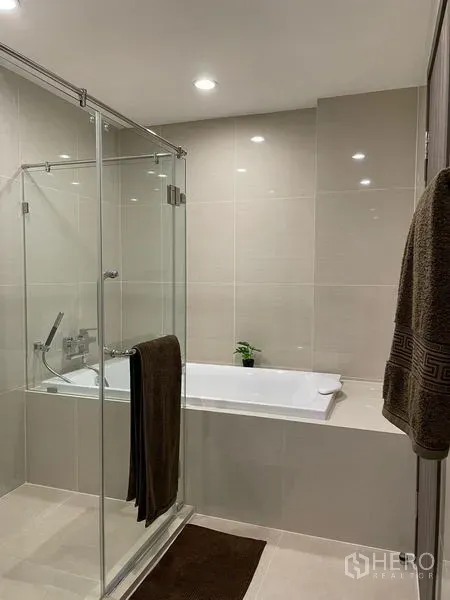 คอนโด ให้เช่าในBang Na, Bangkok - ห้องน้ำสมัยใหม่ มีฝักบัวกระจกกั้นติดกับอ่างอาบน้ำ ปูกระเบื้องโทนเบจ