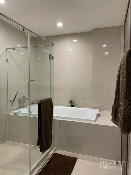 คอนโด ให้เช่าในBang Na, Bangkok - ห้องน้ำสมัยใหม่ มีฝักบัวกระจกกั้นติดกับอ่างอาบน้ำ ปูกระเบื้องโทนเบจ