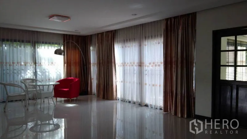 Detached House for rent - Living room corner with red armchair, small table and sheer curtains.