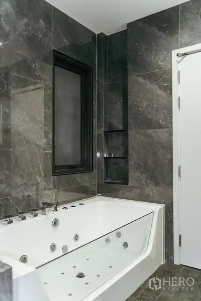 Detached House for sale in Sai Mai, Bangkok - Bathroom clad in marble tiles with a white jacuzzi bathtub and black framed window.