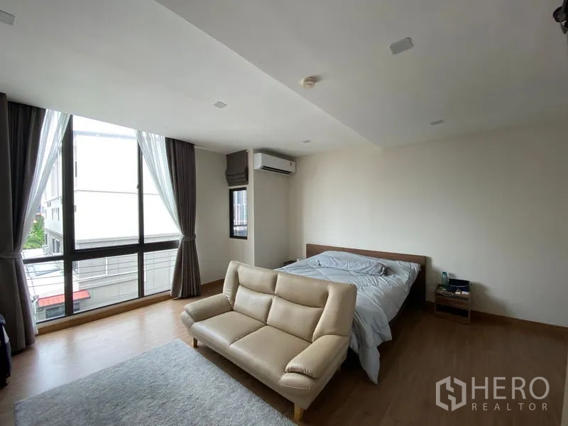Townhouse for rent in Suan Luang, Bangkok - Spacious master bedroom with large corner windows, air conditioning and a sofa.