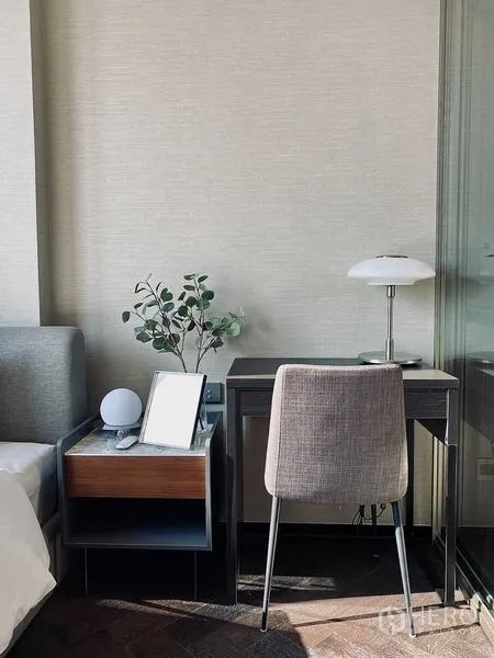 Condominium for rent in Khlong Toei, Bangkok - Compact work nook beside the bed with desk, chair, table lamp, and greenery.