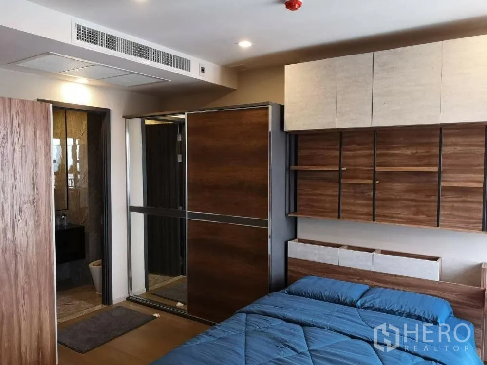 คอนโด for rent in Watthana, Bangkok - ห้องนอนผ้าปูสีน้ำเงิน พร้อมชั้นบิวท์อินไม้และตู้เสื้อผ้าบานเลื่อนกระจกข้างทางเข้าห้องน้ำ