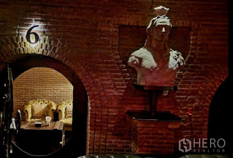 Retail Space for rent - Brick-arched lounge with a stone bust and tufted sofas in a dim, speakeasy-style retail space.