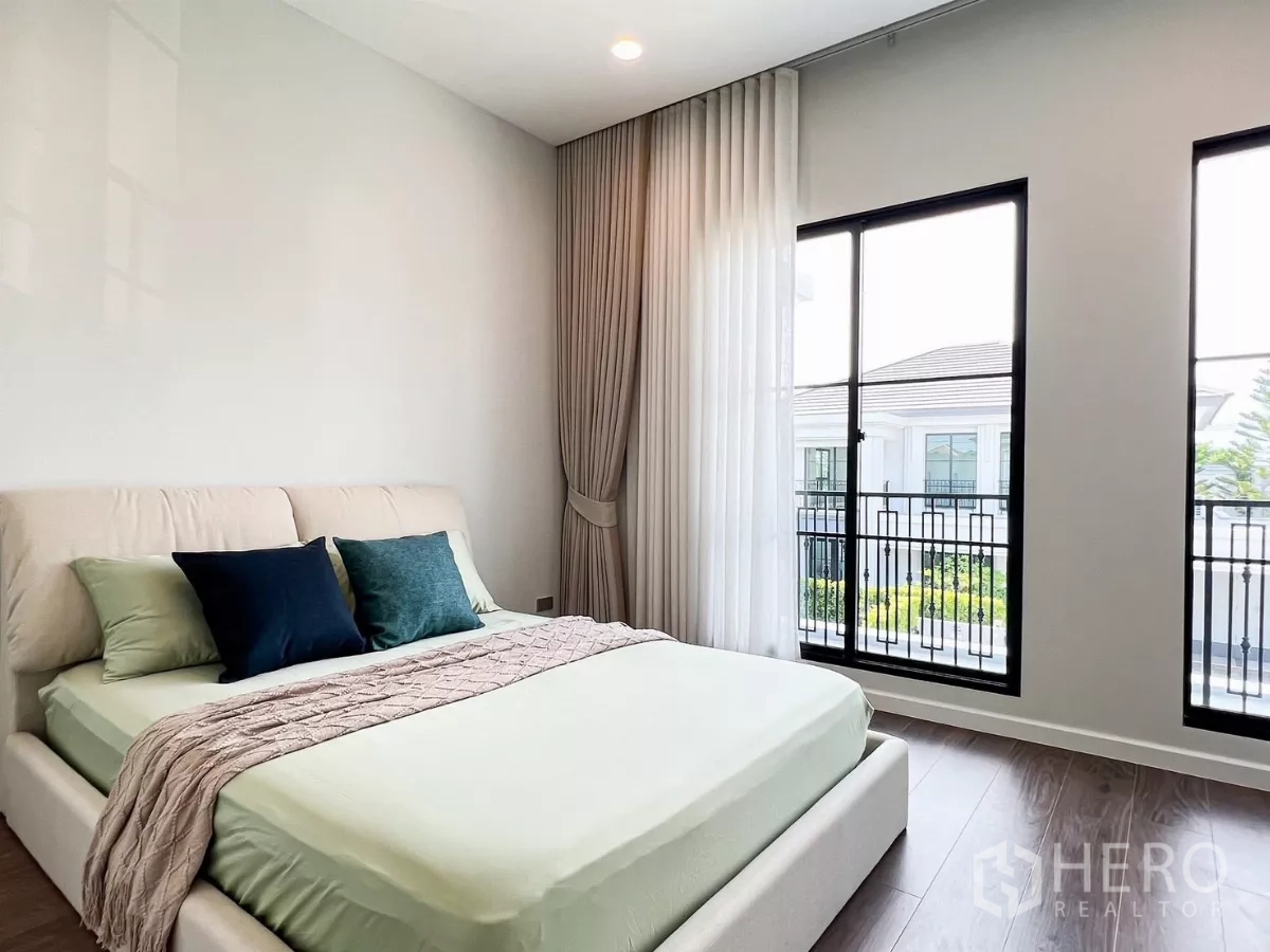 Detached House for rent in Khan Na Yao, Bangkok - Bedroom with soft green bedding, floor-to-ceiling windows and balcony railing view.