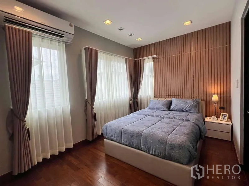 独立式住宅 出租或出售在Lat Krabang, Bangkok - 卧室配蓝色床品、转角窗与木质条纹背景墙。