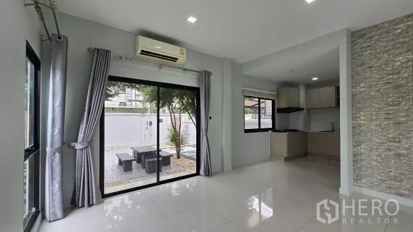 Townhouse for rent or sale in Saphan Sung, Bangkok - Living and dining zone with sliding glass doors to a private garden and adjacent kitchen.