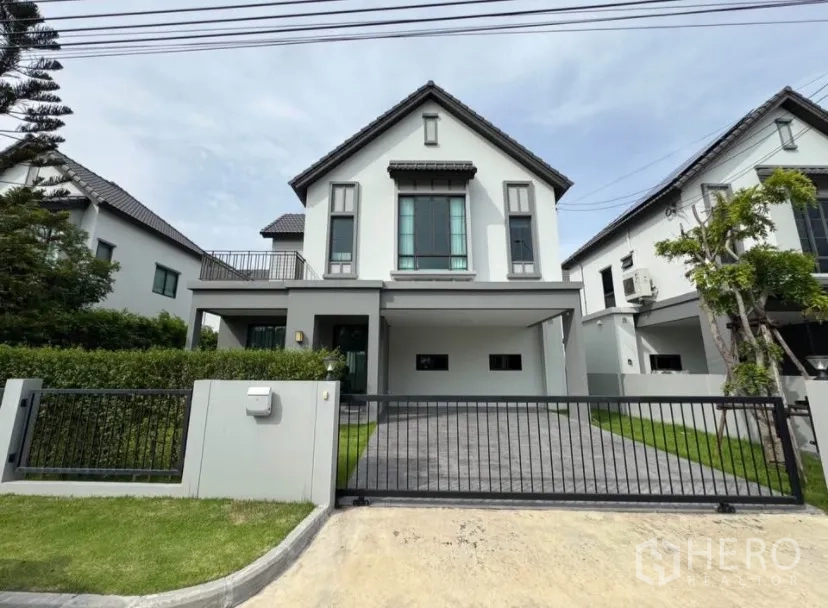 Detached House for rent or sale in Lat Krabang, Bangkok - Front facade of modern detached house with gated driveway, carport, hedges, and neat lawn.