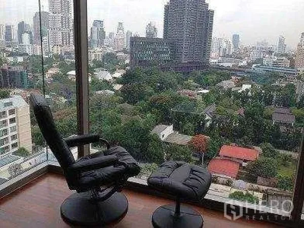 Condominium for rent - Recliner and ottoman by corner windows overlooking green neighborhoods and high‑rise towers.