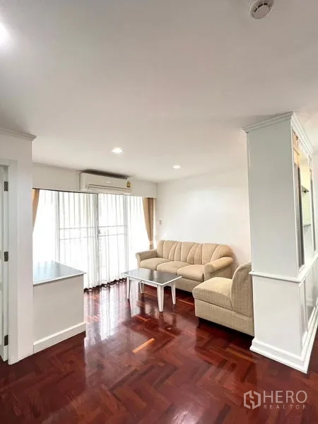 公寓 出租在Watthana, Bangkok - 明亮客厅，米色沙发，落地推拉门通阳台与抛光木地板，近BTS澎蓬站。