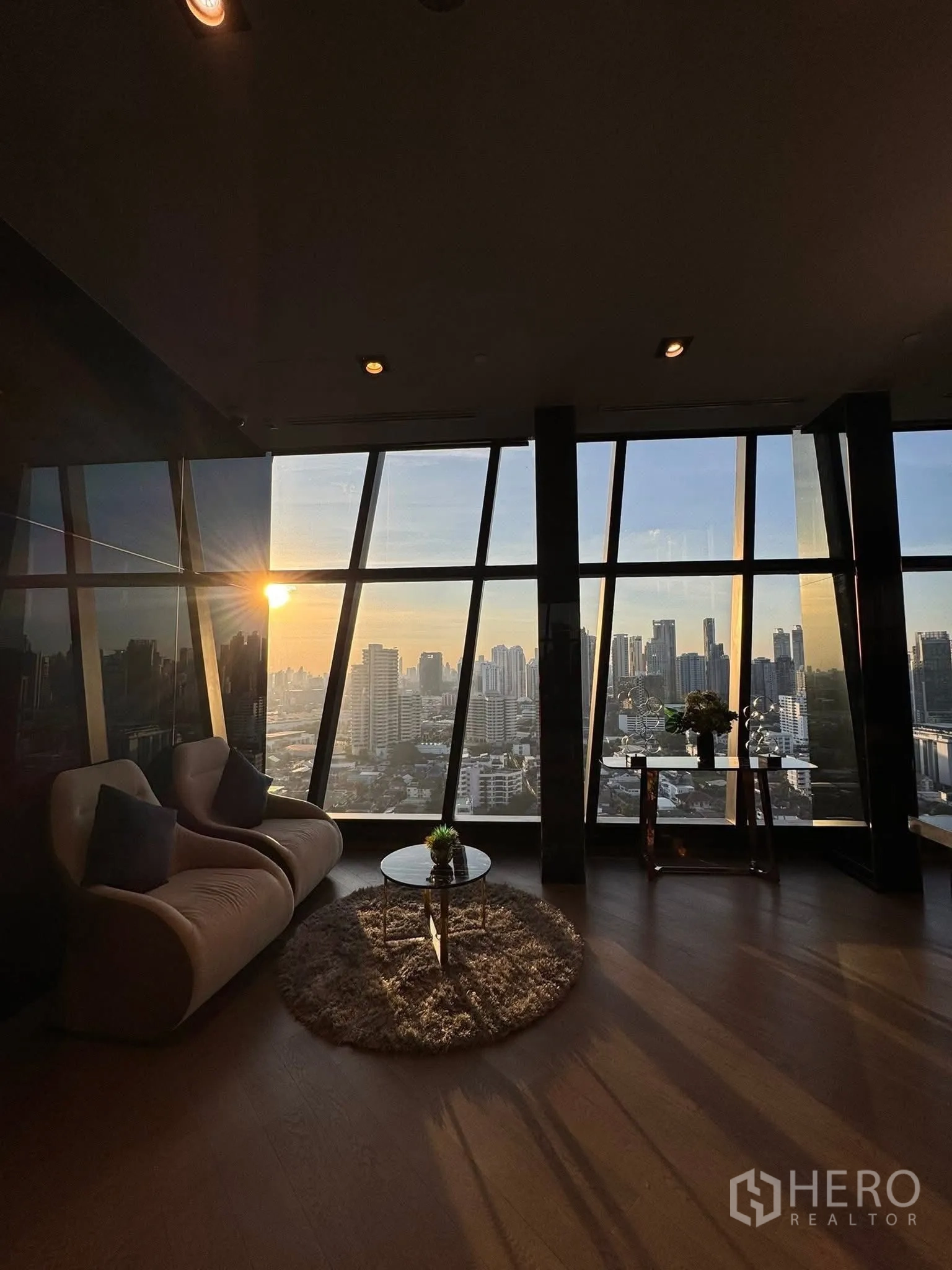 Condominium for rent in Khlong Toei, Bangkok - Cozy seating corner with sofa and coffee table overlooking a sunset skyline.