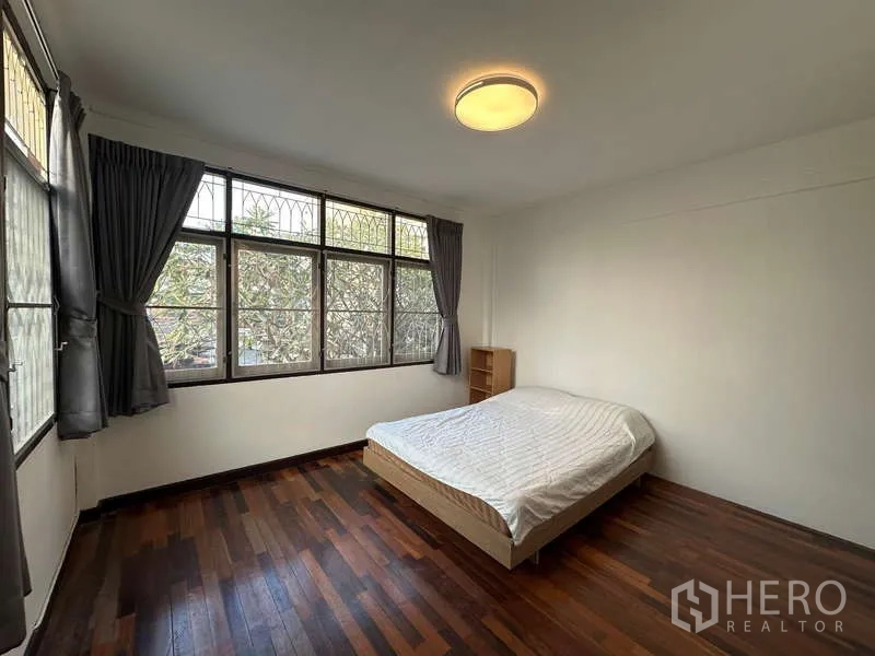Home Office for rent in Din Daeng, Bangkok - Corner bedroom with wide windows overlooking trees, dark wood floor and queen bed.