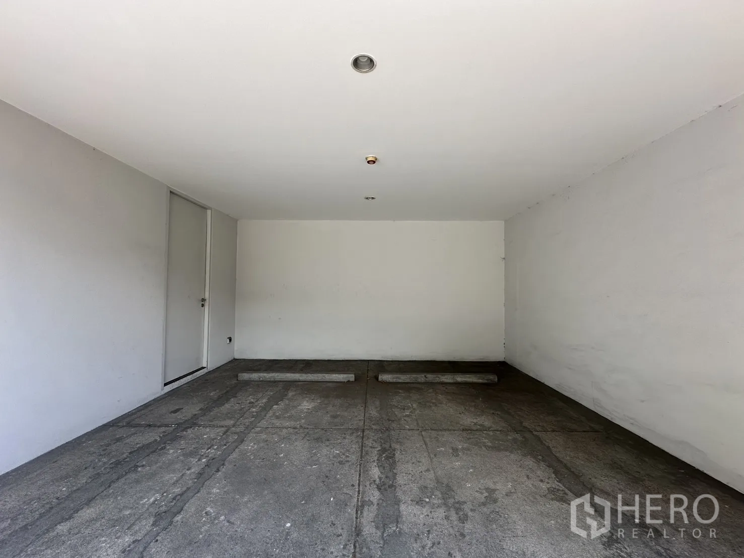 โฮมออฟฟิศ for rent in Phra Khanong, Bangkok - ที่จอดรถในร่มมีช่องจอดสองคัน ผนังสีขาวและประตูด้านข้าง.