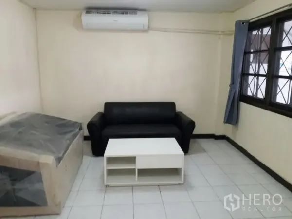 联排别墅 出租在Watthana, Bangkok - 简约客厅，黑色沙发、白色茶几、瓷砖地面与壁挂空调