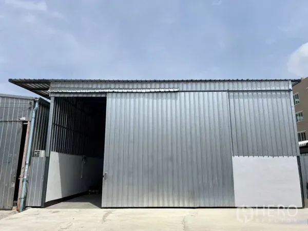 Warehouse for rent in Saphan Sung, Bangkok - Metal-clad warehouse exterior with large sliding door and concrete loading yard under clear sky in Saphan Sung, Bangkok