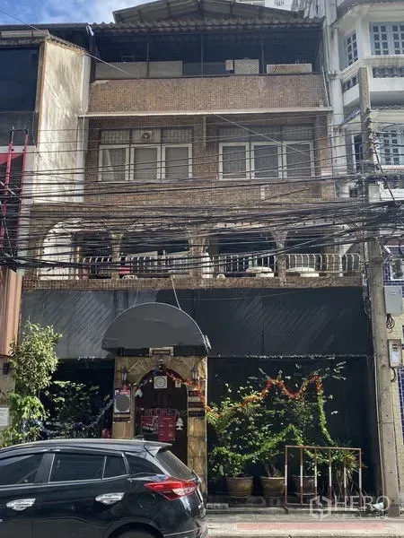 อาคารพาณิชย์ ขายในKhlong Toei, Bangkok - มุมมองด้านหน้าอาคารพาณิชย์อิฐหลายชั้น ระเบียงโค้ง หน้าร้าน กระถางต้นไม้ และสายไฟเหนือถนน ในเขตคลองเตย