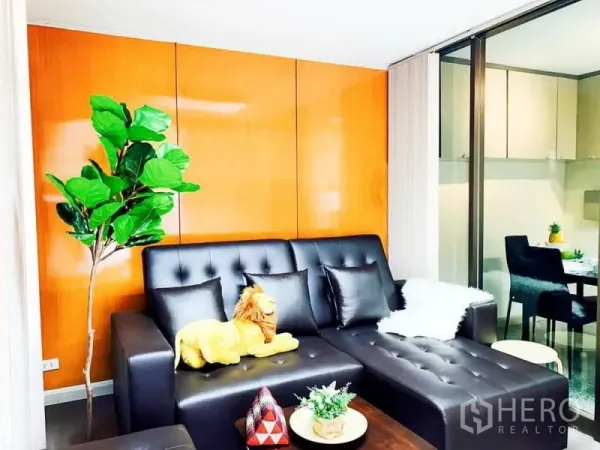 Home Office for rent in Khlong Toei, Bangkok - Cozy lounge with black leather sectional sofa, wood accent wall and indoor plant.