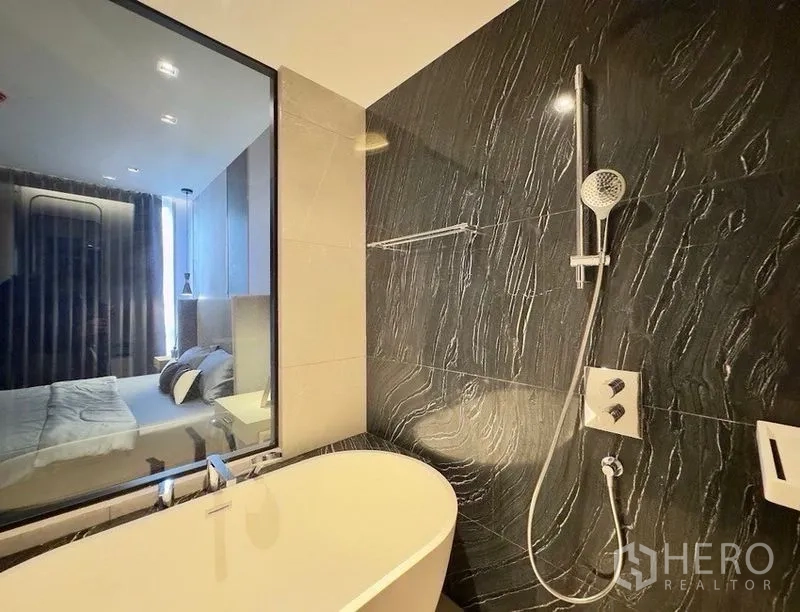 Condominium for rent or sale in Watthana, Bangkok - Bathroom with freestanding bathtub beside a window and a wall-mounted shower on dark tiles.