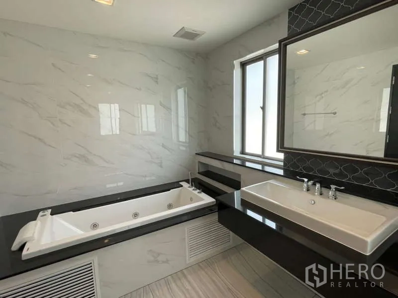 Detached House for rent or sale in Lat Krabang, Bangkok - Modern bathroom with a built-in whirlpool tub, long countertop and marble-look tiles.