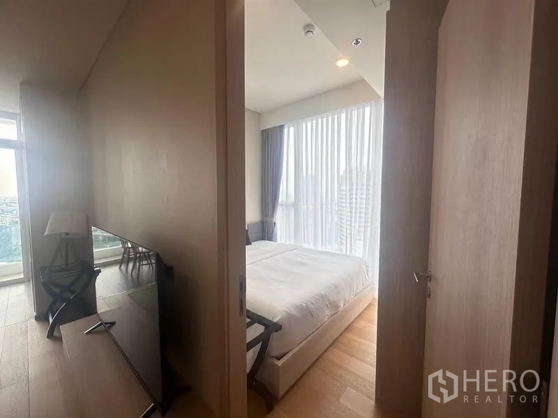 Condominium for rent - Hallway leading to a bright bedroom with floor-to-ceiling curtains and bed, TV visible along the corridor.