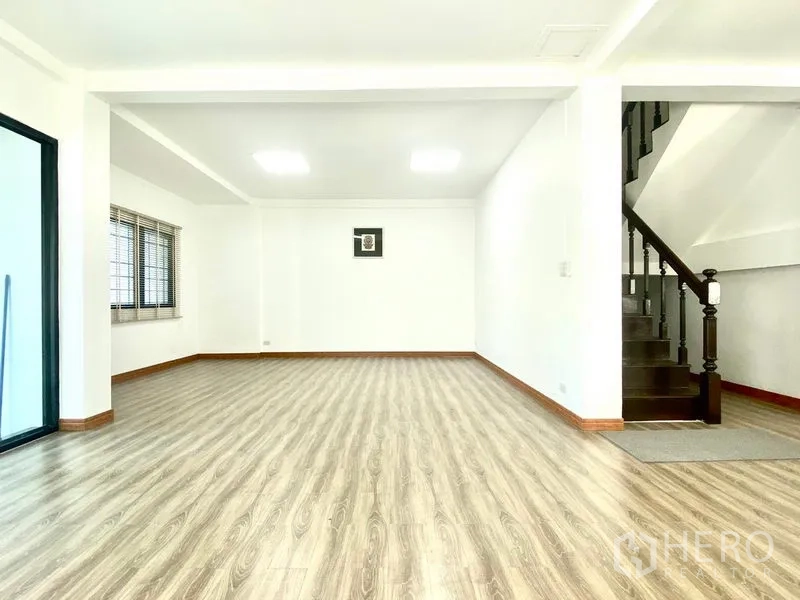 Townhouse for rent in Prawet, Bangkok - Bright open-plan living room with wood-look floors and a staircase.
