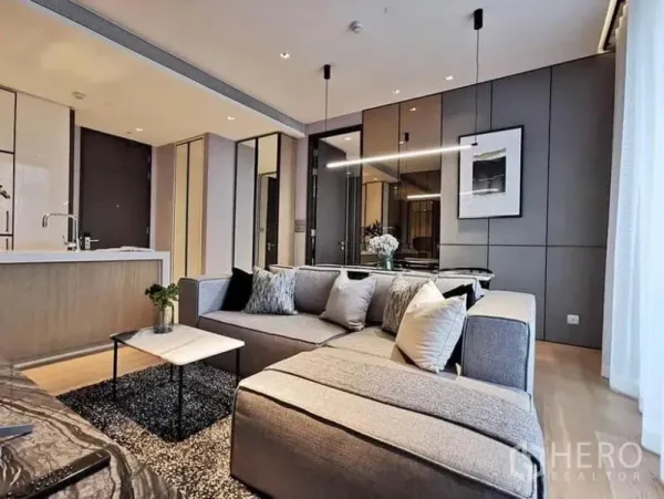 Condominium for rent in Khlong Toei, Bangkok - L-shaped sofa with pendant lighting and mirrored wall panels next to kitchen island
