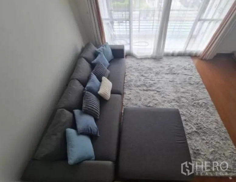 联排别墅 出租在Prawet, Bangkok - 俯视角度的灰色沙发与大地毯，旁有通阳台的玻璃门。