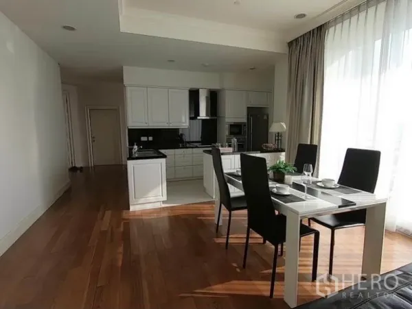 Condominium for rent in Watthana, Bangkok - Dining table for four next to white cabinetry kitchen and full-height balcony glazing.
