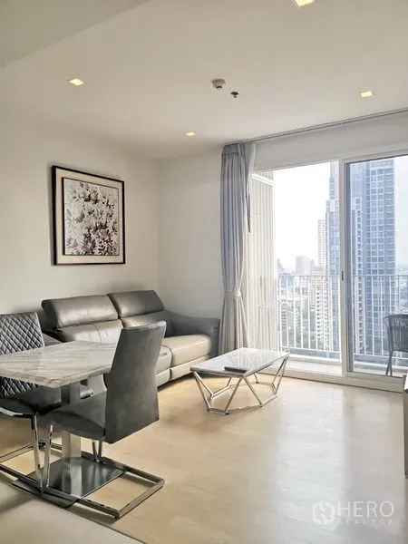 Condominium for rent in Watthana, Bangkok - Bright living room with leather sofa, marble coffee table and balcony offering a Bangkok skyline view.