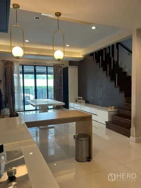 联排别墅 出租在Khlong Toei, Bangkok - 开放式厨房与餐区，吊灯、岛台和木楼梯，后方为推拉门通向庭院