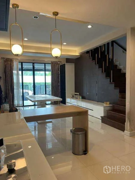 联排别墅 出租在Khlong Toei, Bangkok - 开放式厨房与餐区，吊灯、岛台和木楼梯，后方为推拉门通向庭院