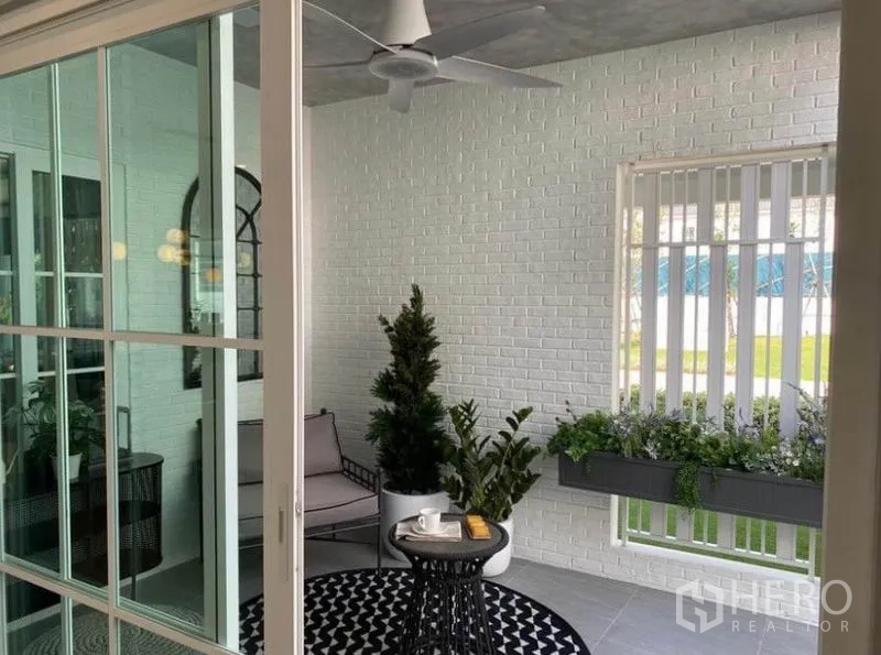 บ้าน ให้เช่าในBang Phli, Samut Prakan - ซันรูมหรือเฉลียงปิด ผนังอิฐขาว พัดลมเพดาน และต้นไม้กระถาง