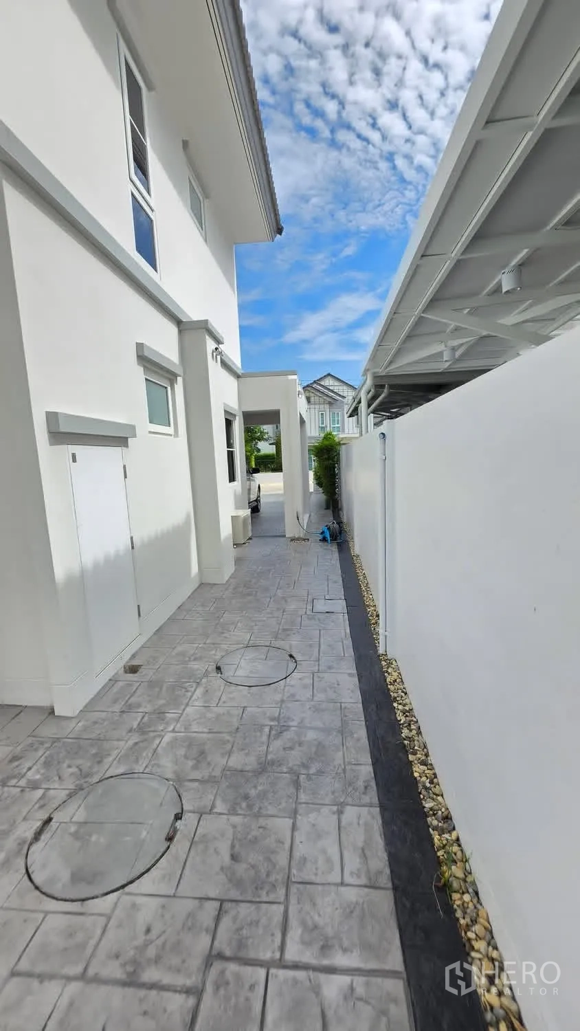 独栋房屋 for rent in Bang Phli, Samut Prakan - 白色独栋别墅侧边通道，仿石地砖与局部遮棚。