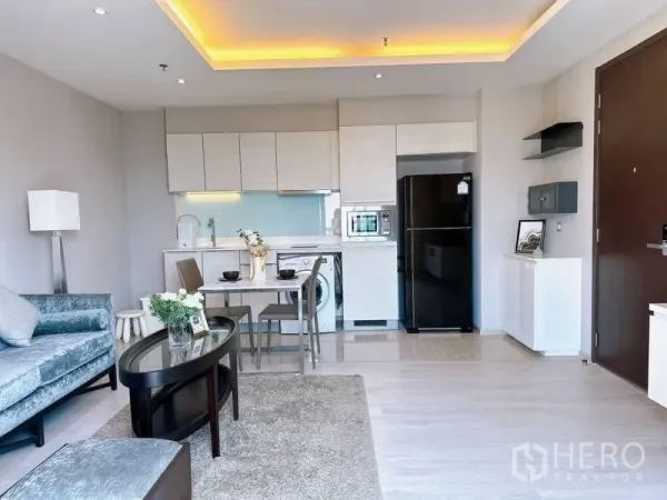 Condominium for rent in Watthana, Bangkok - Open-plan living room with grey sofa, dining table and full kitchen with cove lighting.