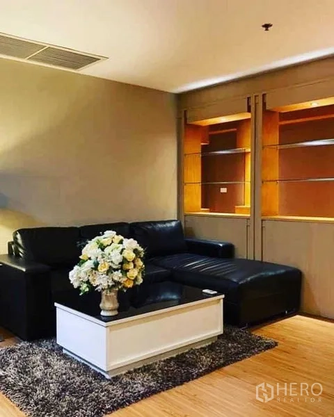 Condominium for rent in Watthana, Bangkok - Warm living room featuring a black leather sectional, white coffee table and illuminated shelving.