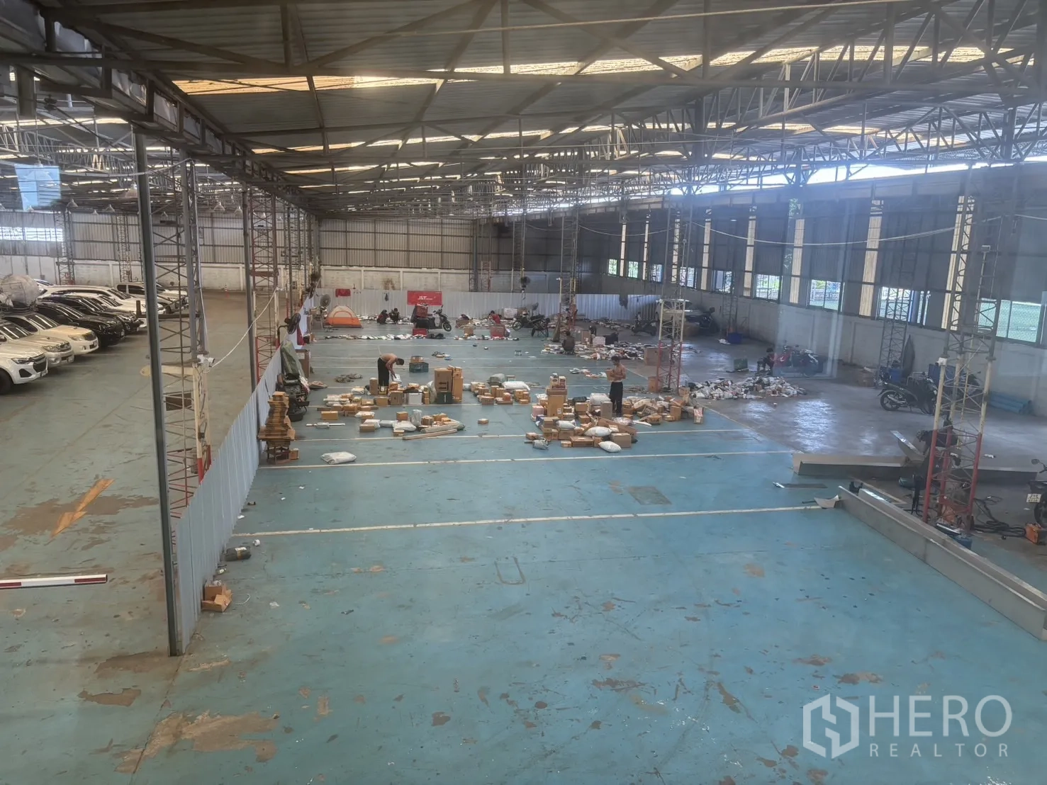 工厂 for rent or sale in Bang Sao Thong, Samut Prakan - 宽敞仓库内部，钢结构屋顶与采光板，蓝色地坪，侧边有车辆停放。