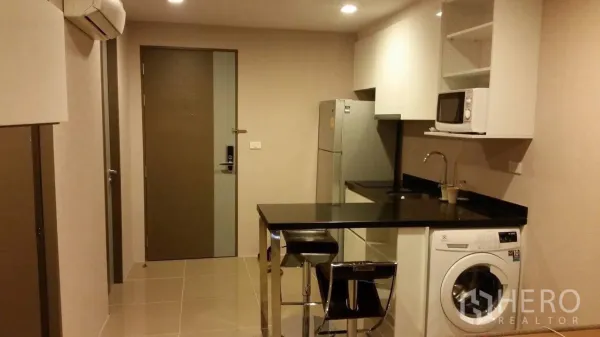 公寓 出租在Watthana, Bangkok - 开放式厨房，黑色石材台面吧台，配冰箱、微波炉和滚筒洗衣机。