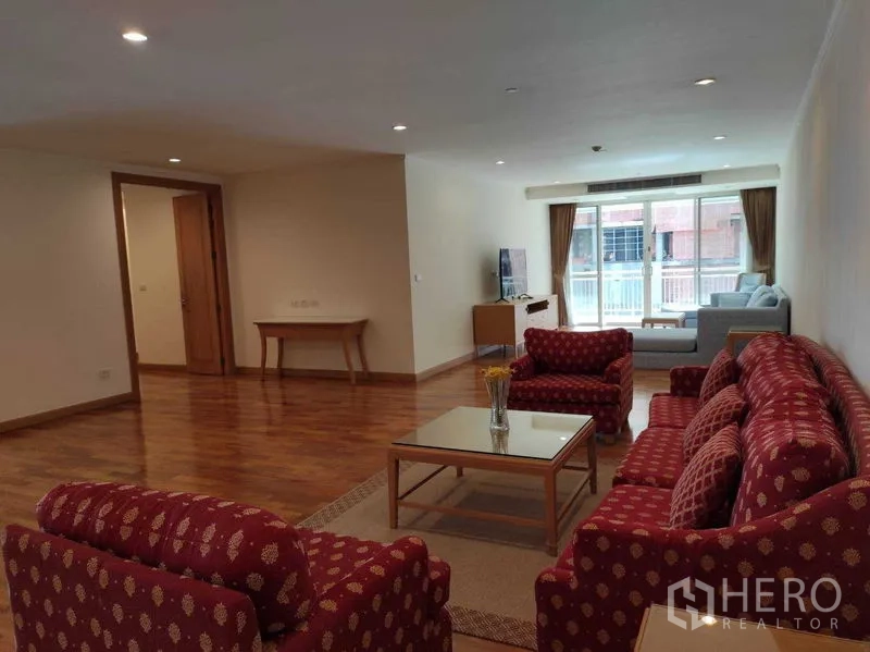 Condominium for rent in Khlong Toei, Bangkok - Secondary lounge with patterned red sofa set, glass coffee table and wide window to the balcony.