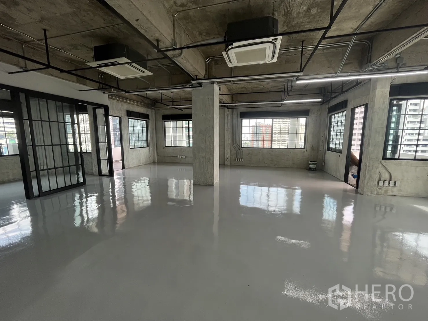 办公空间 出租在Khlong Toei, Bangkok - 宽敞工作区，混凝土立柱、吊装灯具与天花式空调，窗外城市景观。